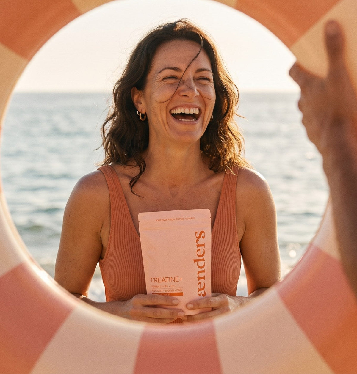 Lachende Frau am Meer mit einer Packung Aenders Creatine+: Kreatin für Frauen ab 40 und ab 50